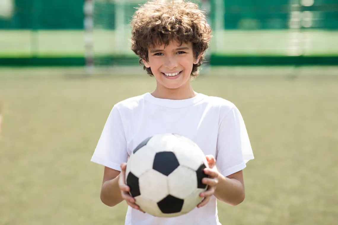 A boy holds a soccer ball standing in a field